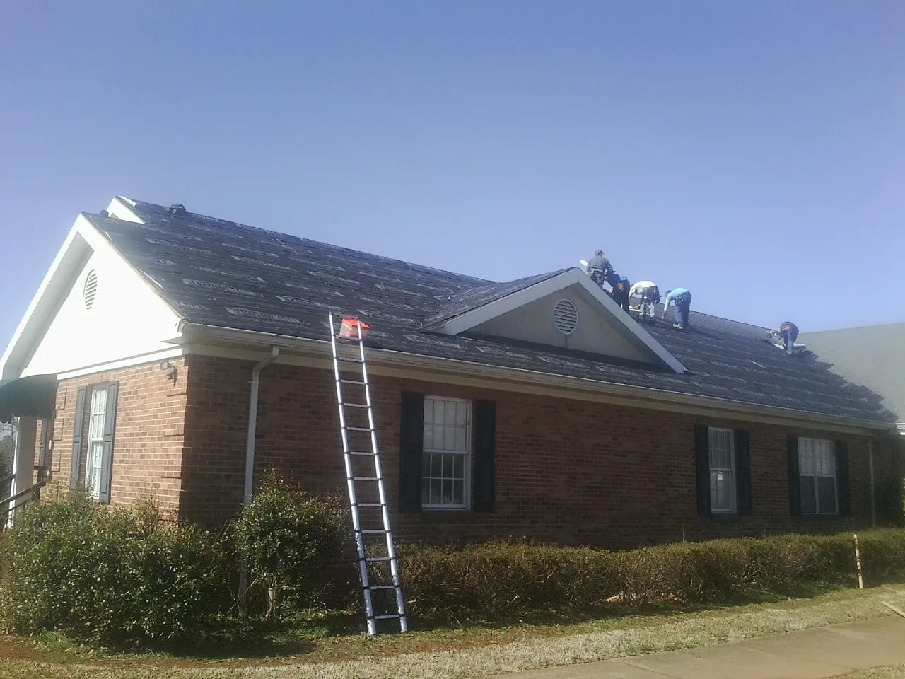 Crew tearing shingles off a brick ranch roof with a ladder set — Emergency Roof Repair work by our crew in Gordonville