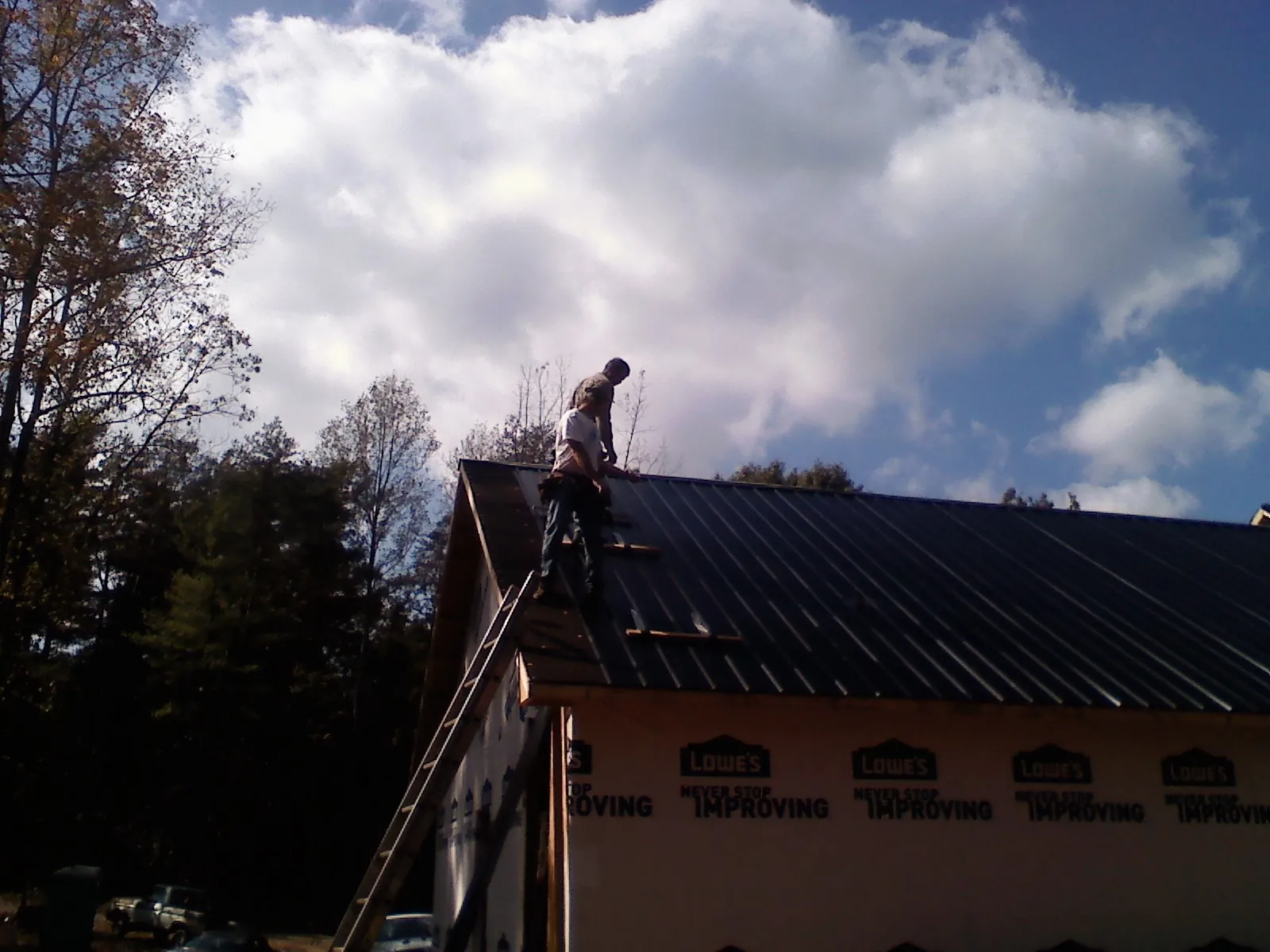 Roofer fastening dark metal panels high against a cloudy sky, from a Roof Inspection job in Gordonville