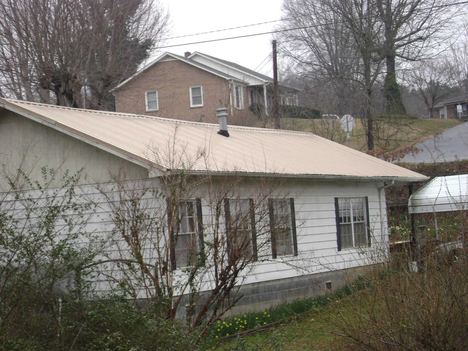 Tan metal roof on a white sided house set into a hillside — Commercial Roofing by Roofing Brothers in Gordonville